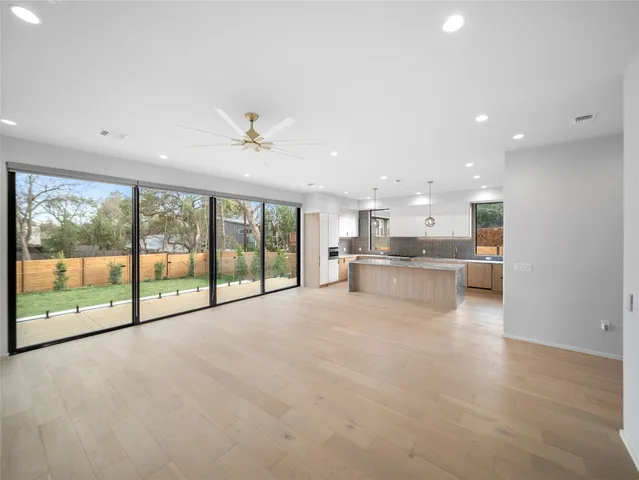 a view of an empty room with a kitchen view and a large window