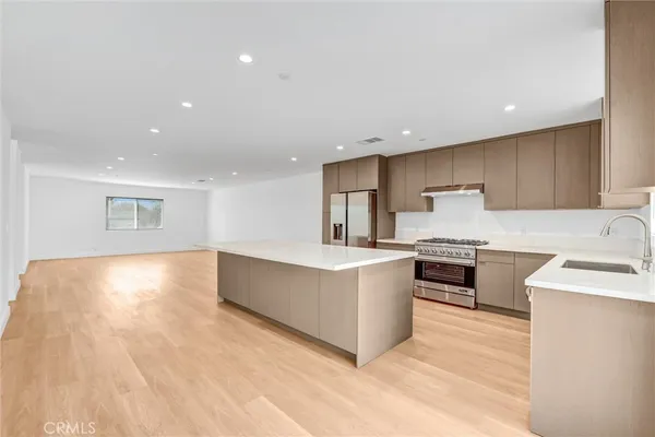 a large kitchen with stainless steel appliances granite countertop a large counter top a stove a sink dishwasher and a refrigerator with wooden floor
