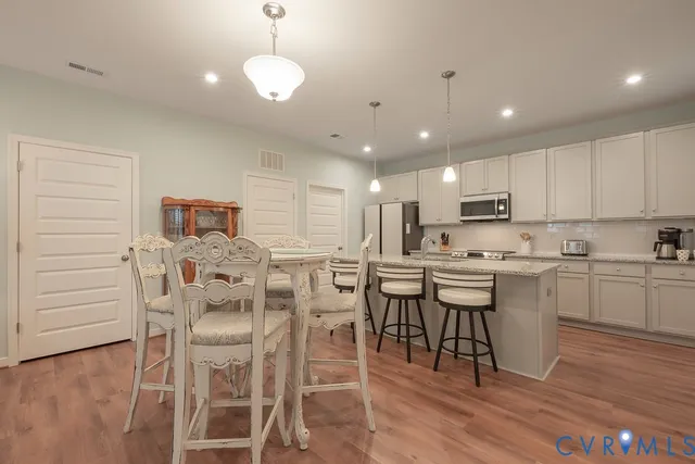 a kitchen with stainless steel appliances kitchen island granite countertop a dining table chairs sink and cabinets