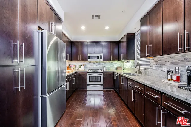 a kitchen with stainless steel appliances granite countertop a refrigerator a sink dishwasher a kitchen island with wooden floor and cabinets