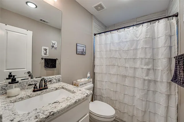 a bathroom with a granite countertop sink a toilet a mirror and shower curtain