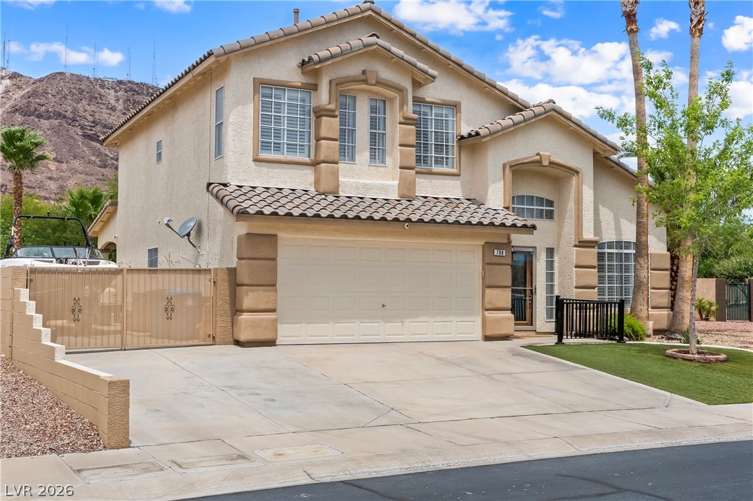 708 Vortex Avenue Henderson, NV 89002 - Photo 5 of 71 A cream-colored stucco home with a tile roof and attached garage stands before a mountain backdrop.