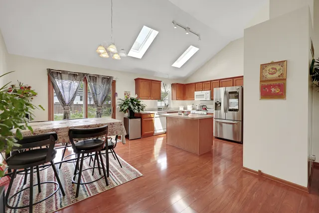 a kitchen with granite countertop a refrigerator a stove a dining table and chairs with wooden floor