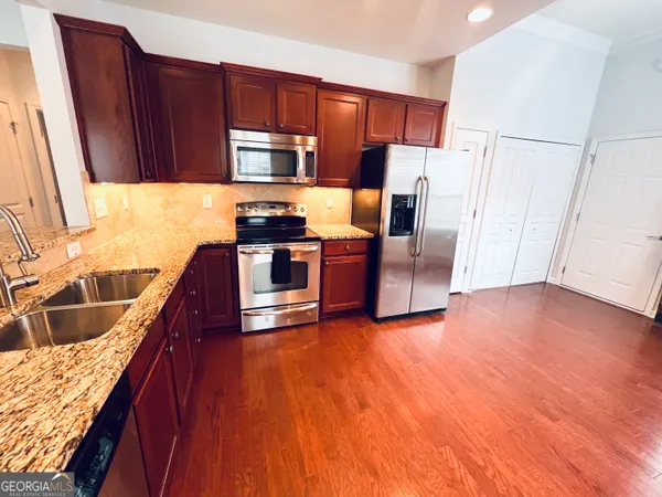 a kitchen with stainless steel appliances granite countertop a refrigerator a stove top oven and a sink with wooden floors