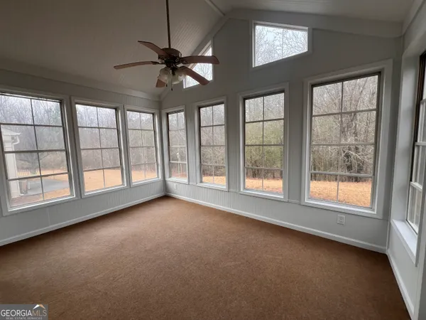 an empty room with chandelier fan and windows