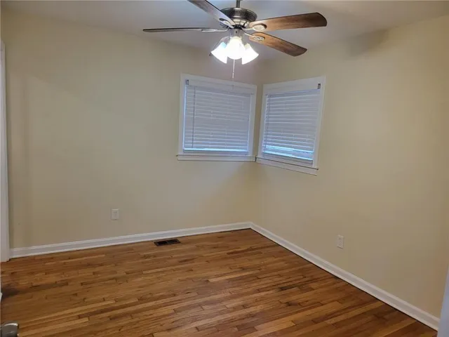 a view of an empty room with wooden floor and a fan