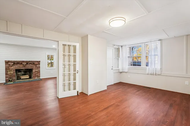 an empty room with wooden floor fireplace and windows
