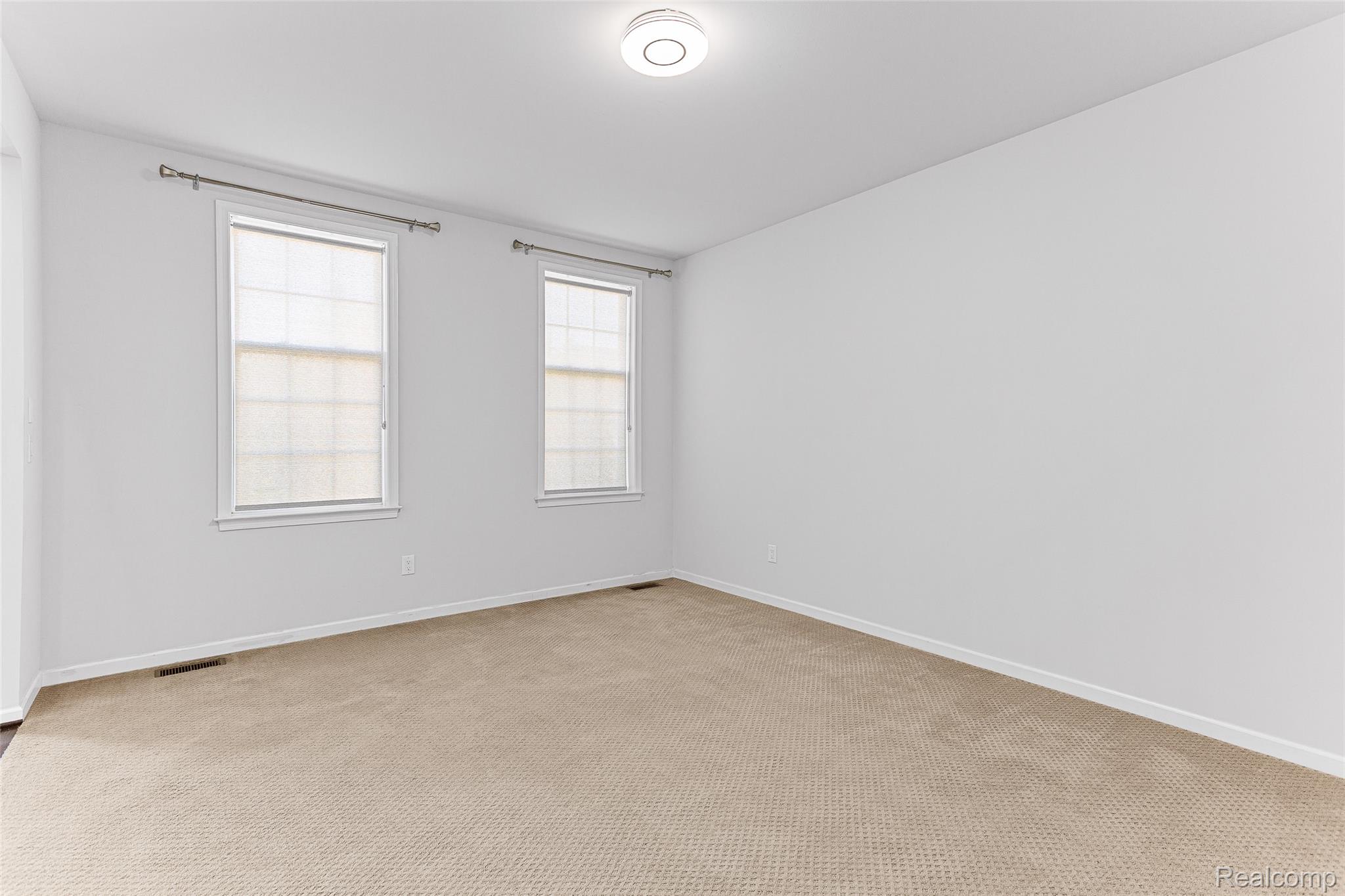 Carpeted flooring, white walls, two windows with window treatments, and a ceiling-mounted light fixture