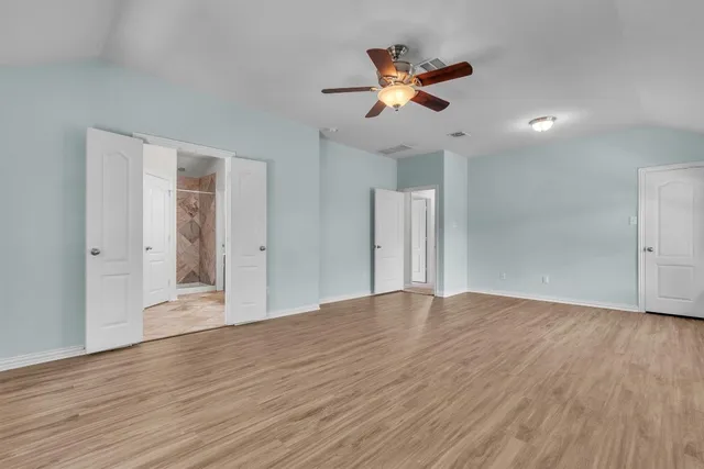 a view of an empty room with wooden floor and a ceiling fan