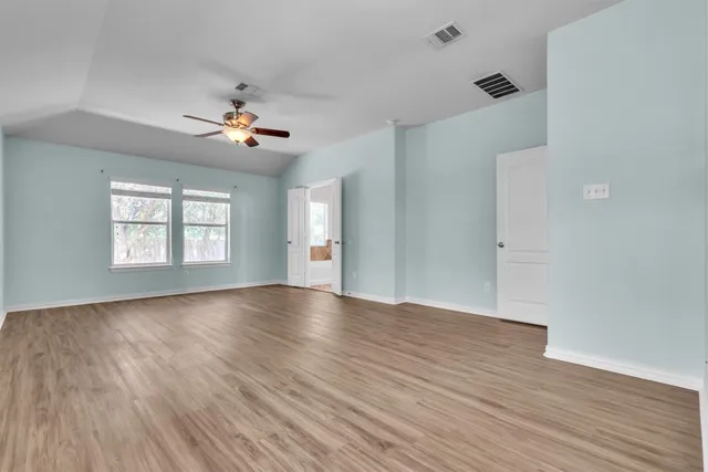 an empty room with wooden floor chandelier fan and windows