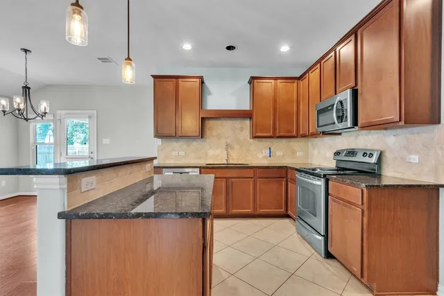 a kitchen with stainless steel appliances granite countertop a sink a stove and a wooden cabinets