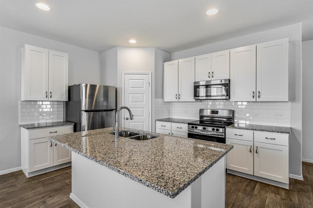 2808 Totley Road Manor, TX 78653 - Photo 2 of 21 Modern kitchen featuring an island with a double sink, stainless steel appliances, white shaker cabinets, granite countertops, and a subway tile backsplash