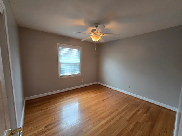 an empty room with wooden floor ceiling fan and windows