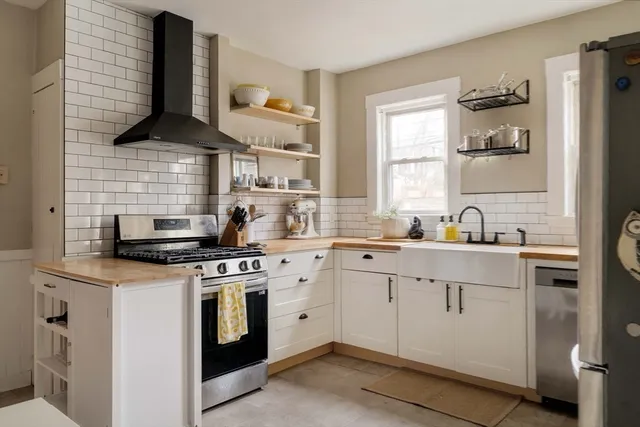 a kitchen with stainless steel appliances a refrigerator a sink a stove and white cabinets with wooden floor