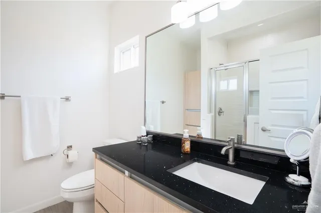 a bathroom with a granite countertop sink a toilet a mirror and shower