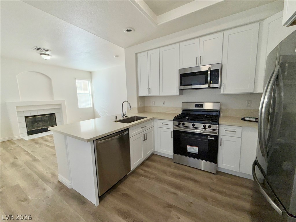 9729 Trail Rider Drive Las Vegas, NV 89117 - Photo 8 of 26 A well-appointed kitchen features stainless steel appliances, pristine white cabinetry, and wood-look flooring, seamlessly connected to a living space with a fireplace.