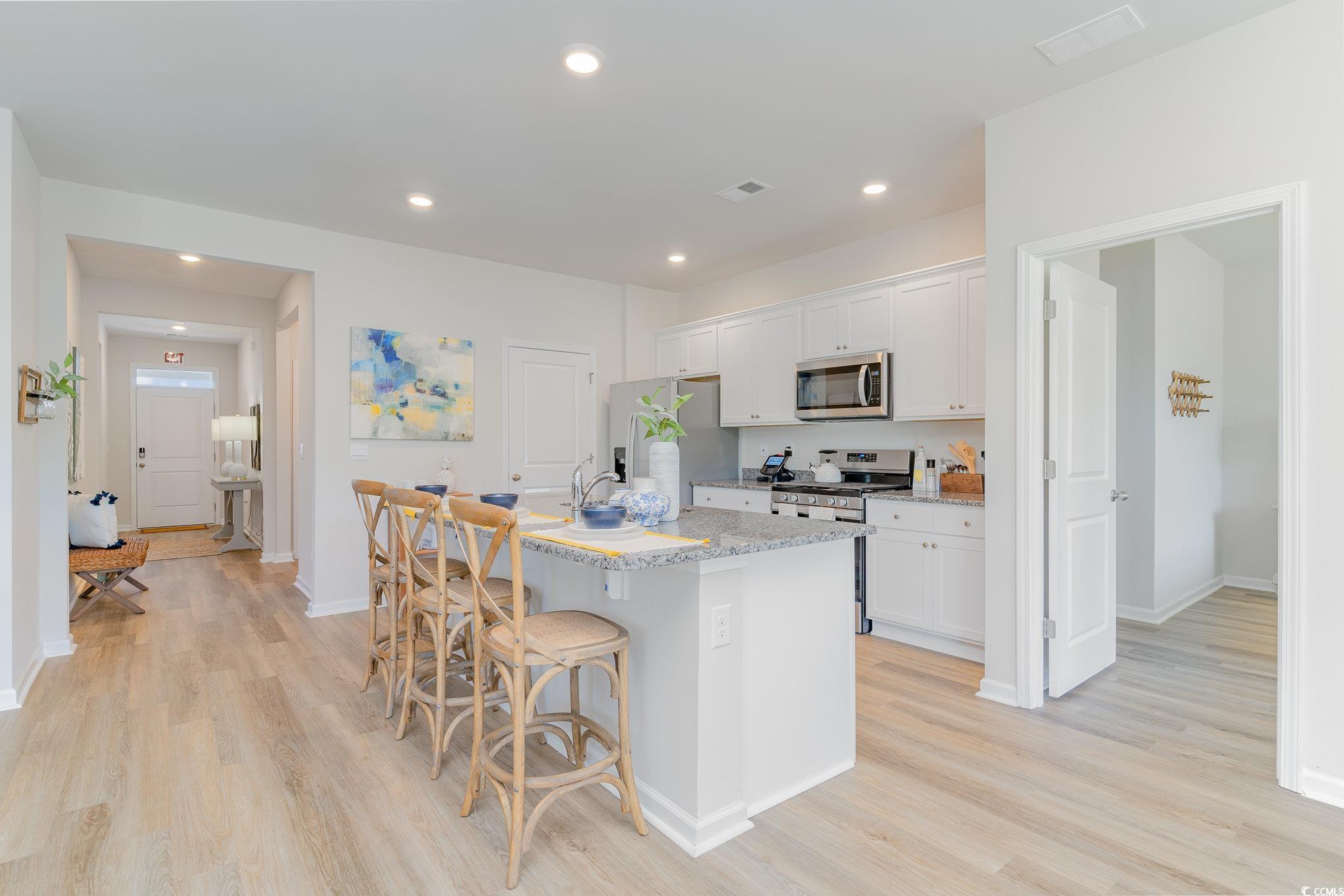 7366 Meadow Walk Loop Loris, SC 29569 - Photo 9 of 20 Kitchen with appliances with stainless steel finishes, a center island with sink, light wood-style flooring, a breakfast bar area, and white cabinetry