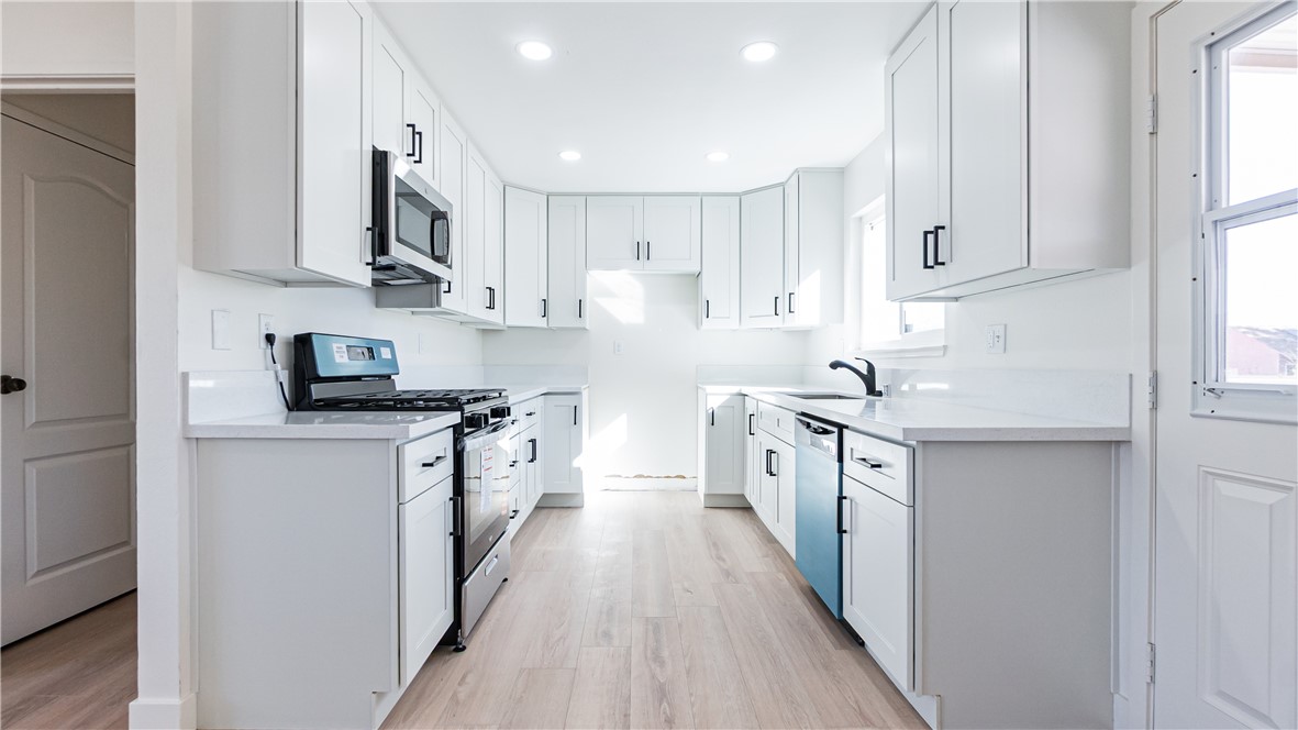 9293 Guava Avenue Hesperia, CA 92345 - Photo 5 of 32 a kitchen with stainless steel appliances white cabinets a sink dishwasher a stove and a refrigerator with wooden floor