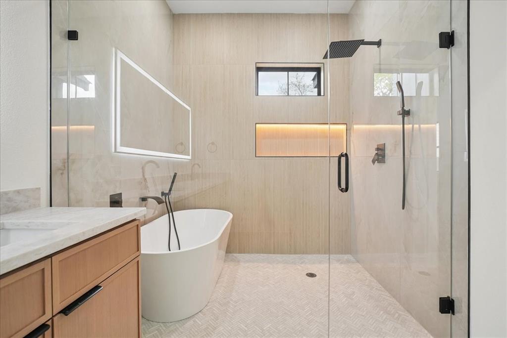 1648 West Wintergreen Road Lancaster, TX 75134 - Photo 17 of 23 Freestanding soaking tub with floor-mounted faucet, illuminated vanity mirror, glass-enclosed shower with rain shower head, and recessed shower niche with accent lighting