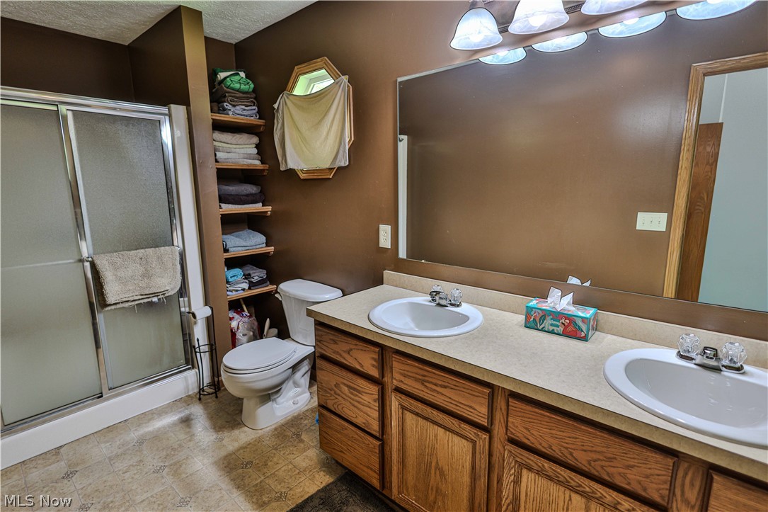 11154 Johnsford Road Southwest Beach City, OH 44608 - Photo 31 of 50 Bathroom featuring a double vanity with wood-finish cabinetry, a large wall-mounted mirror, and a shower with frosted glass doors