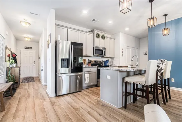 a kitchen with stainless steel appliances granite countertop a refrigerator a stove top oven a sink dishwasher a dining table and chairs with wooden floor