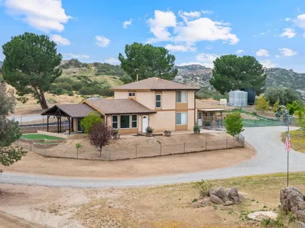 a view of a white house with a yard plants and large tree