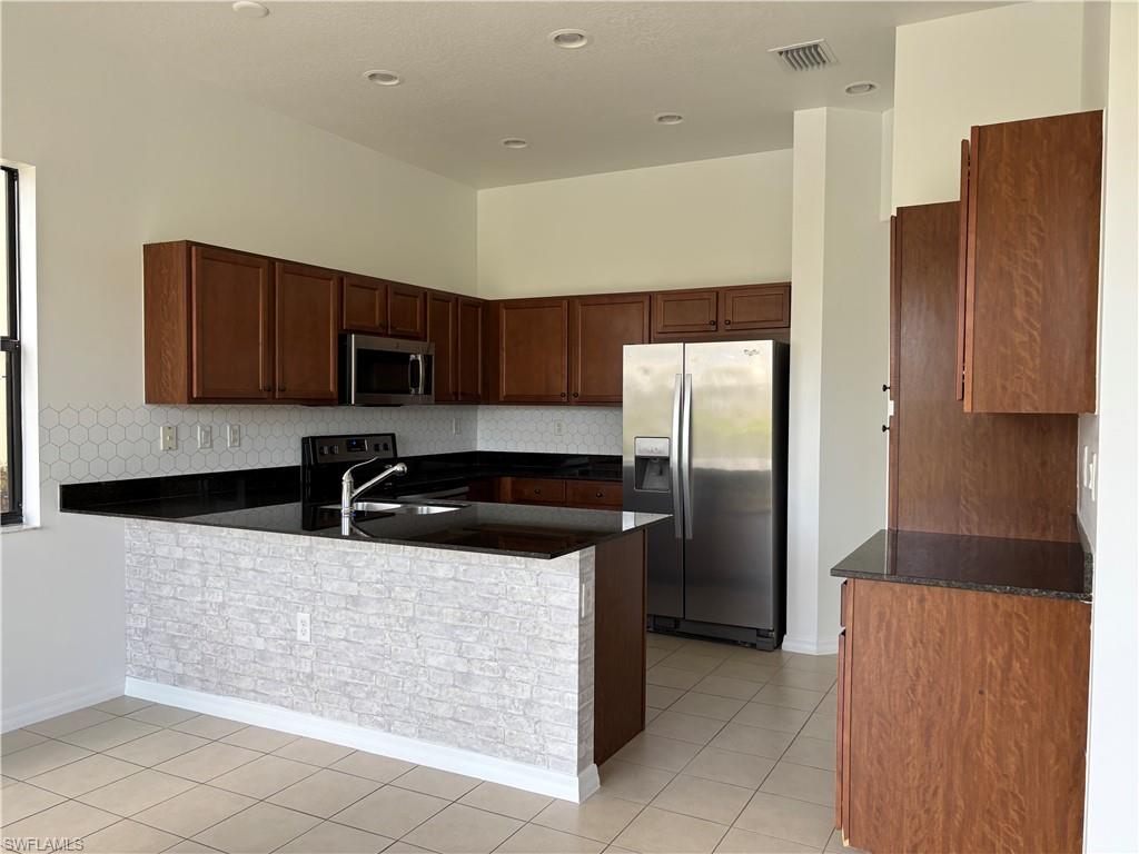 5414 Ferris Avenue Ave Maria, FL 34142 - Photo 3 of 15 Kitchen with appliances with stainless steel finishes, decorative backsplash, a peninsula, light tile patterned flooring, and dark stone countertops