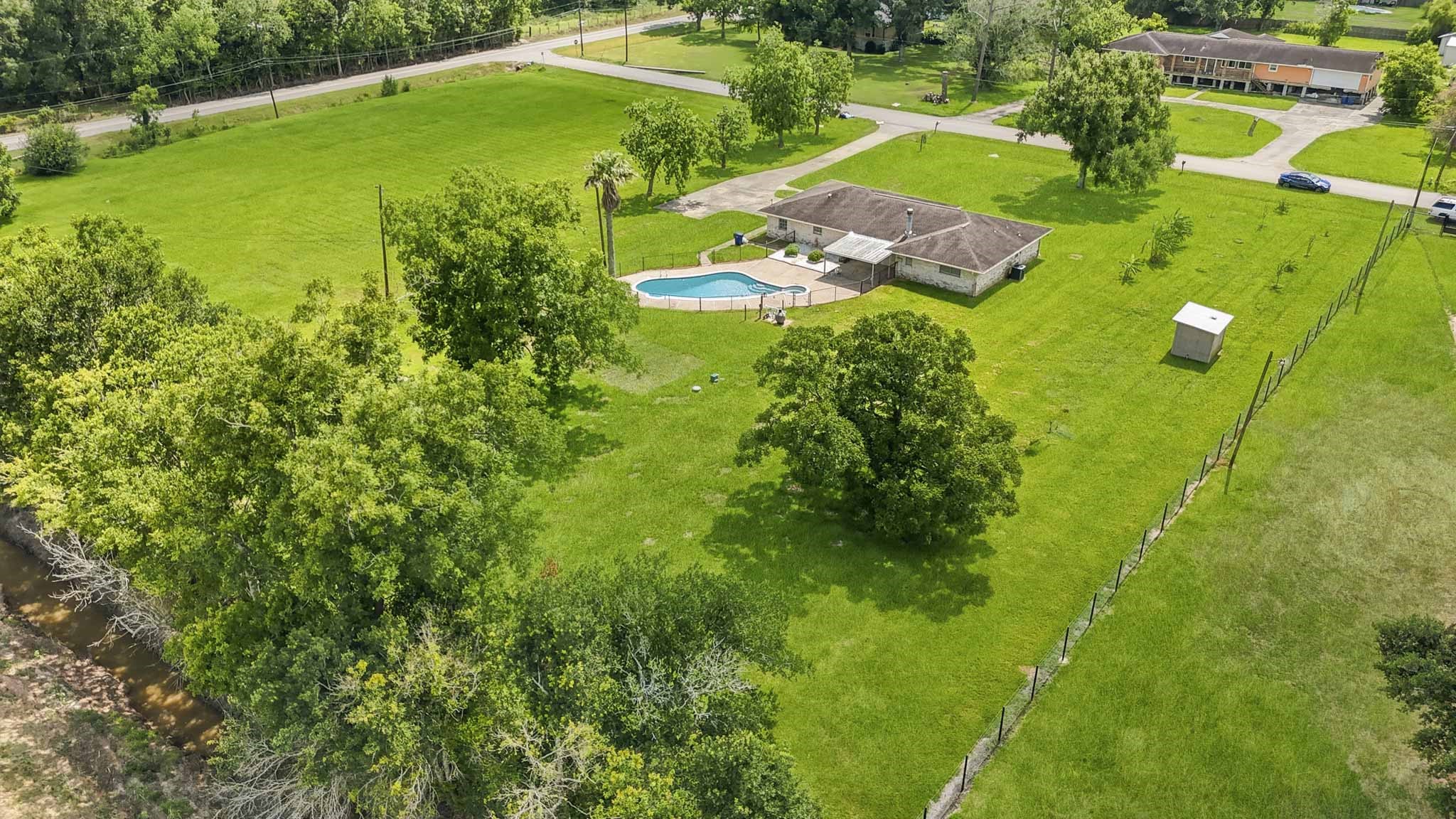 302 Country Road 893 Angleton, TX 77515 - Photo 2 of 26 Beautiful, spacious property featuring a single-story home with a pool, surrounded by lush green lawns and mature trees. The expansive yard offers privacy and ample space, ideal for outdoor activities and relaxation.