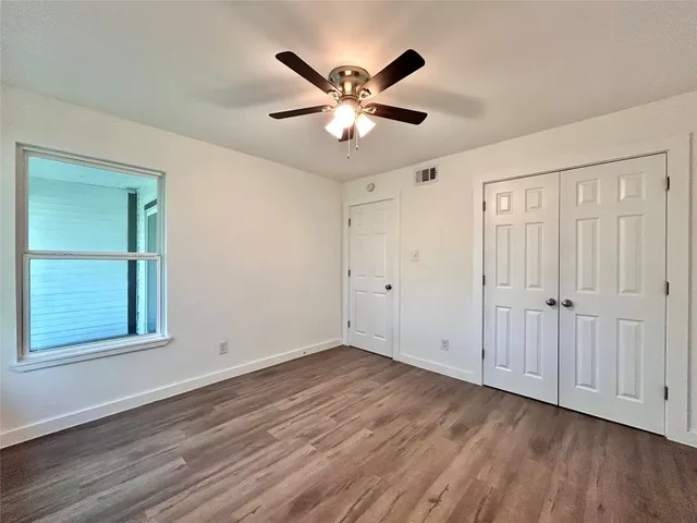 a view of an empty room with wooden floor and a ceiling fan