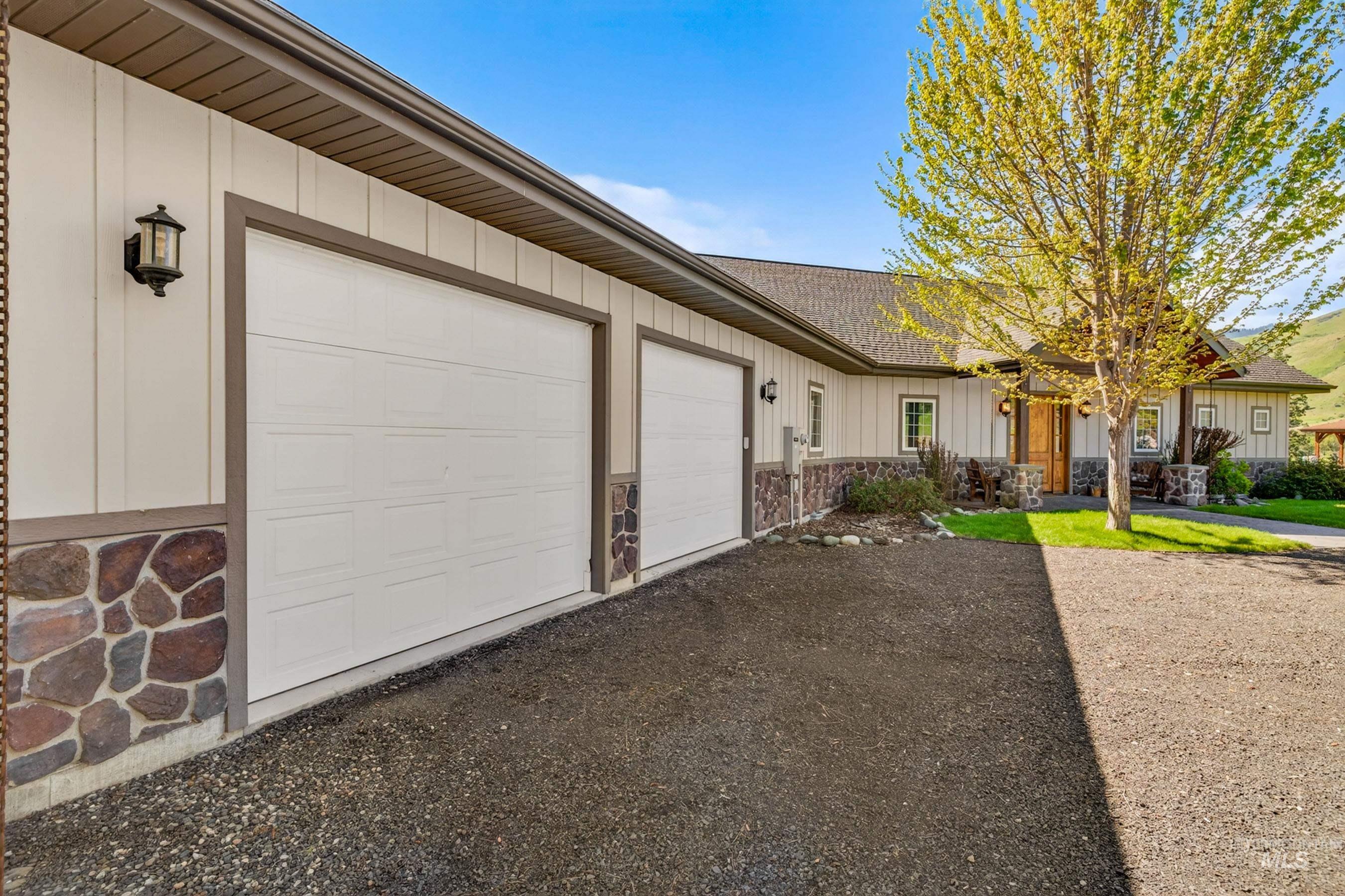 113 Deford Road White Bird, ID 83554 - Photo 37 of 49 Two-car garage with white doors, framed by vertical siding and a stone-clad foundation