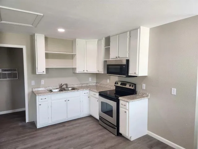 a kitchen with stainless steel appliances a sink dishwasher a stove and a microwave oven on wooden floor