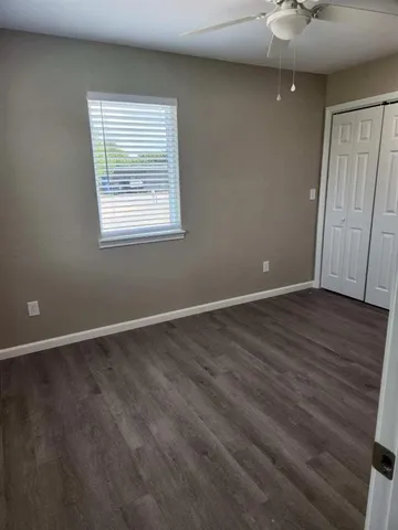 an empty room with wooden floor chandelier fan and windows