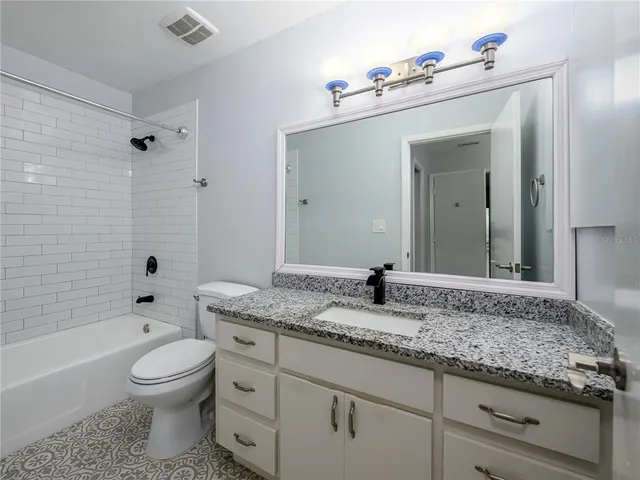 a bathroom with a granite countertop sink a toilet mirror and bathtub
