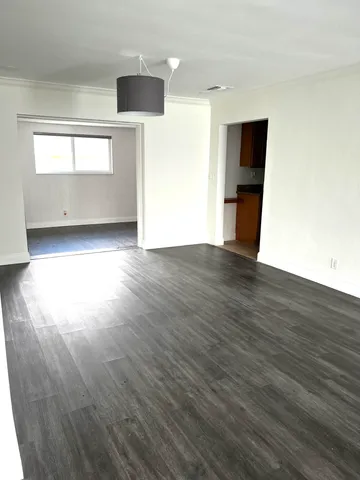a view of empty room with wooden floor and kitchen view
