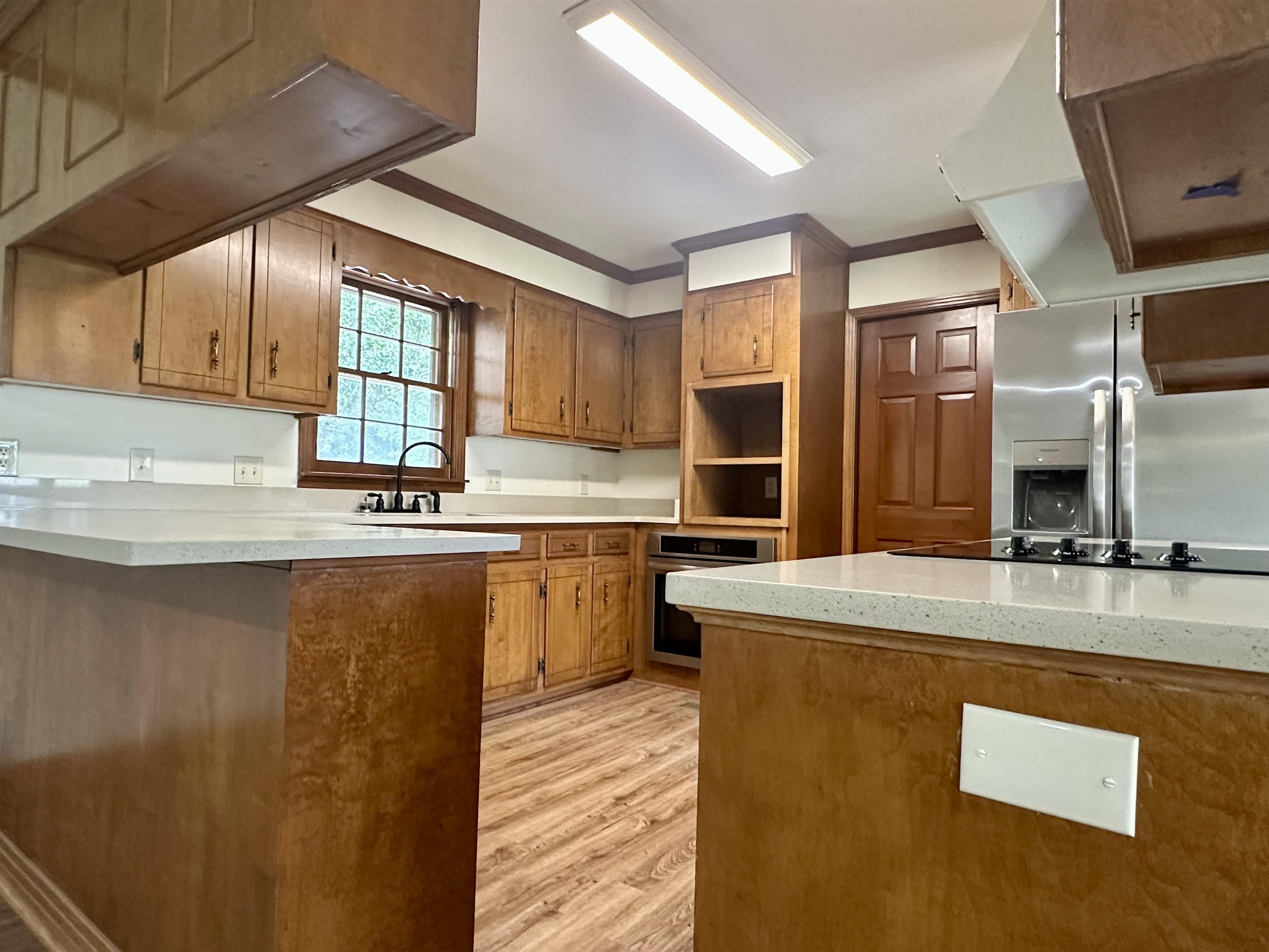 808 West Main Street Adamsville, TN 38310 - Photo 11 of 37 Kitchen featuring appliances with stainless steel finishes, light countertops, light wood-type flooring, brown cabinets, and ornamental molding