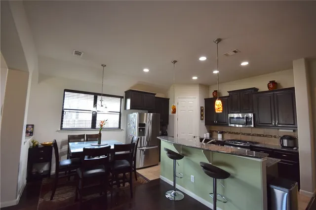 a kitchen with stainless steel appliances granite countertop a refrigerator a stove a sink a dining table and chairs with wooden floor