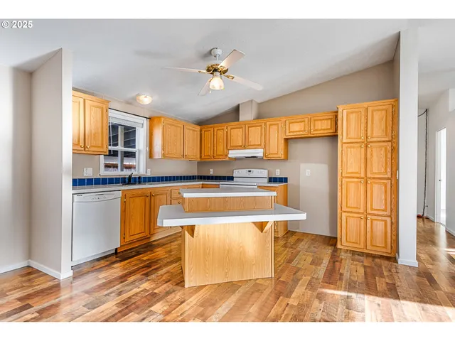 a kitchen with granite countertop a refrigerator a stove a sink dishwasher and white cabinets with wooden floor