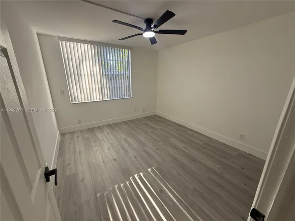 an empty room with wooden floor fan and windows