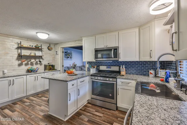 a kitchen with stainless steel appliances granite countertop a stove top oven a sink dishwasher and white cabinets with wooden floor