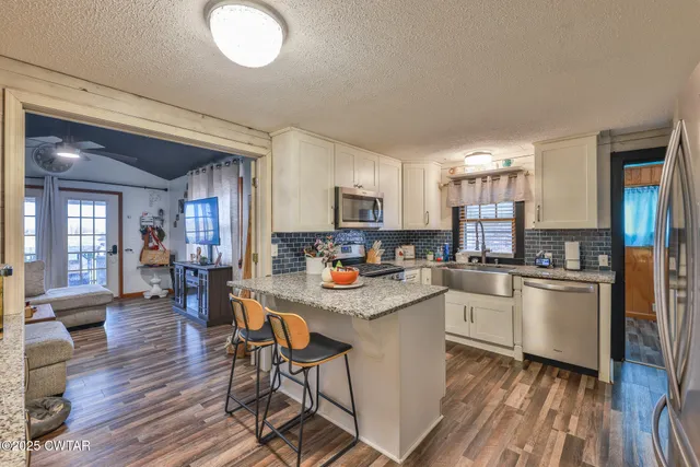 a kitchen with stainless steel appliances granite countertop a stove top oven a sink dishwasher a dining table and chairs with wooden floor