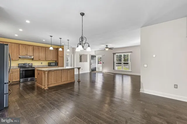 a view of a kitchen with kitchen island a stove a refrigerator wooden floor and a view of living room