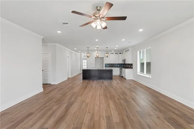 a view of an empty room with wooden floor and a kitchen
