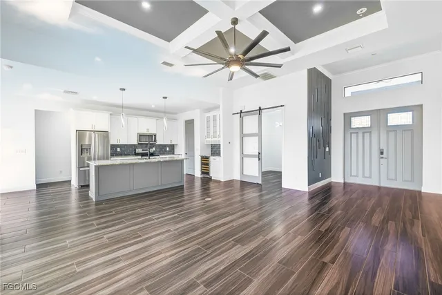a view of an empty room and kitchen view with wooden floor