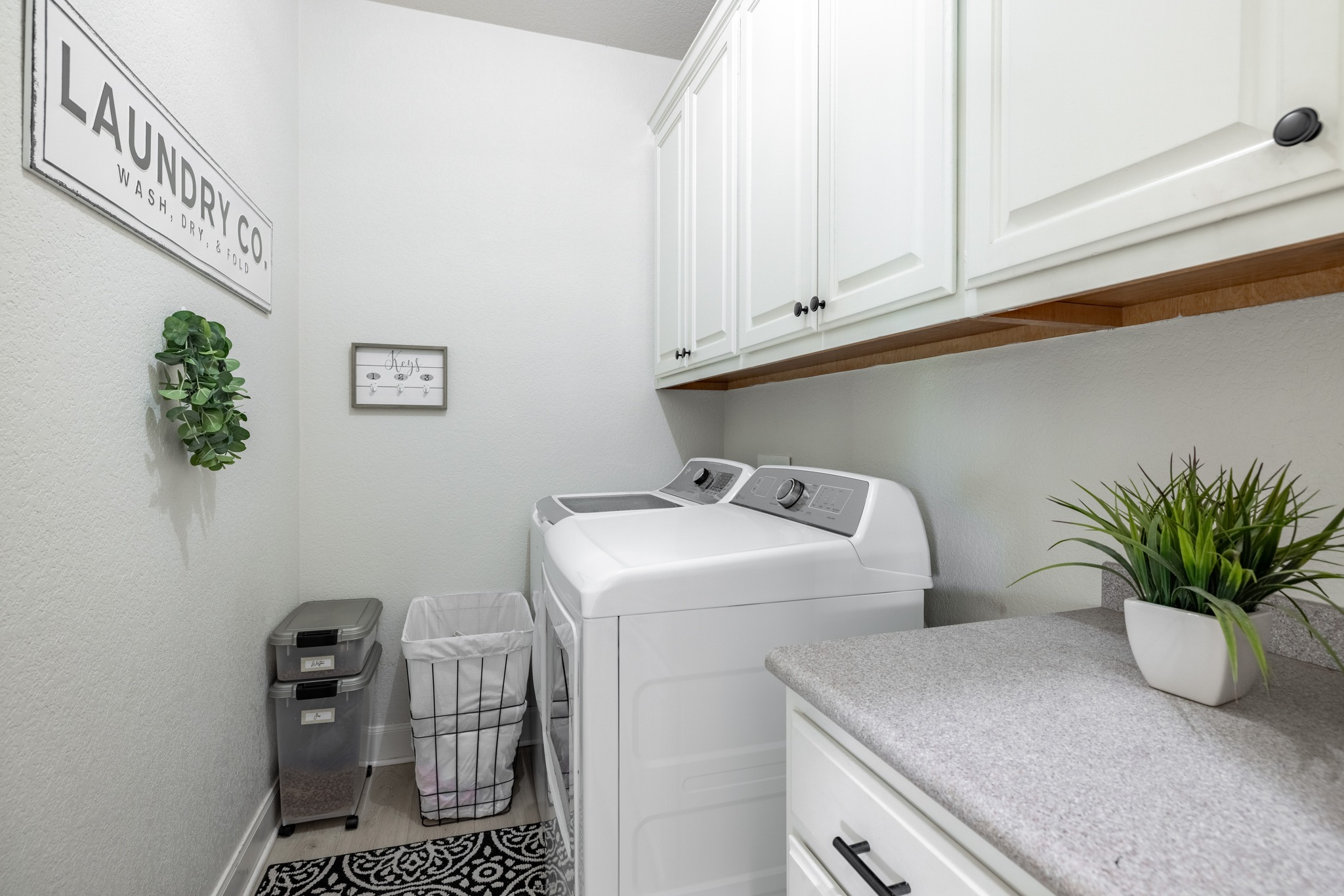 108 Kyle Lane Georgetown, TX 78633 - Photo 18 of 26 Laundry area featuring white cabinetry with black hardware, a grey speckled countertop, and wood-finish flooring
