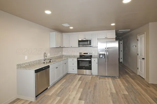 a kitchen with a sink dishwasher a refrigerator and a stove top oven with wooden floor