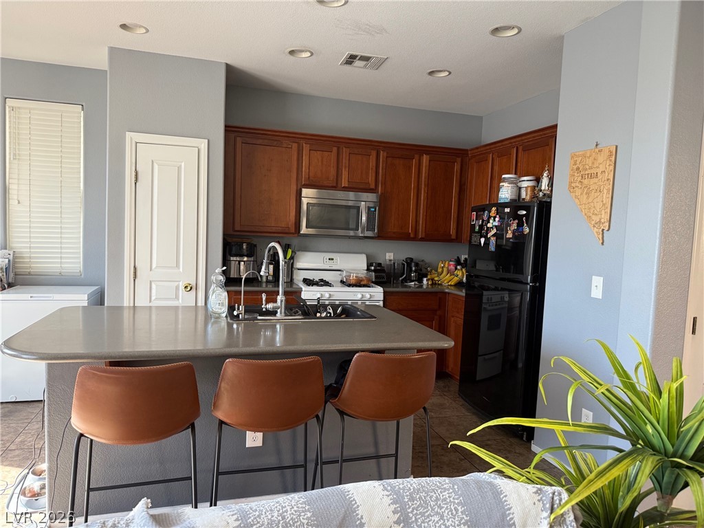 8962 Rutherford Grove Street Las Vegas, NV 89148 - Photo 3 of 16 Kitchen featuring white appliances, a breakfast bar, a center island with sink, dark countertops, and wood finish cabinets