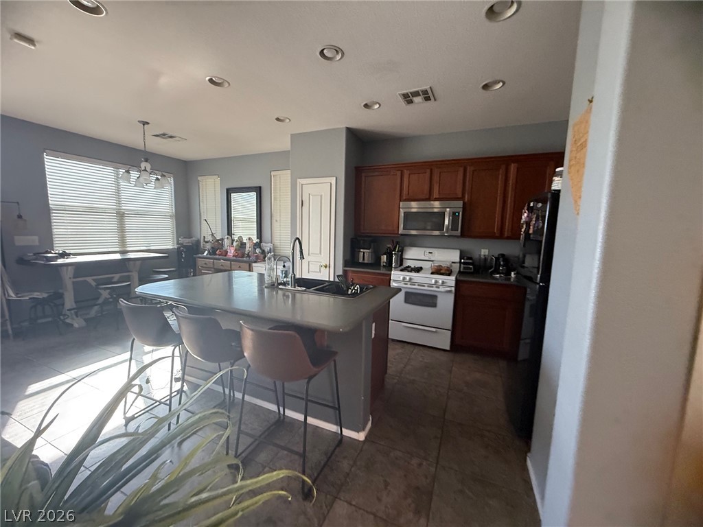 8962 Rutherford Grove Street Las Vegas, NV 89148 - Photo 4 of 16 Kitchen featuring white range with gas cooktop, decorative light fixtures, dark countertops, stainless steel microwave, and a breakfast bar