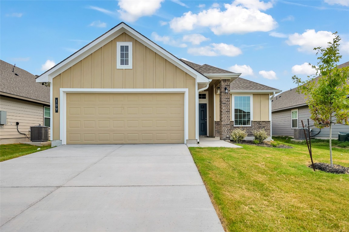 View of front of property with board and batten siding, driveway, an attached garage, a front yard, and roof with shingles