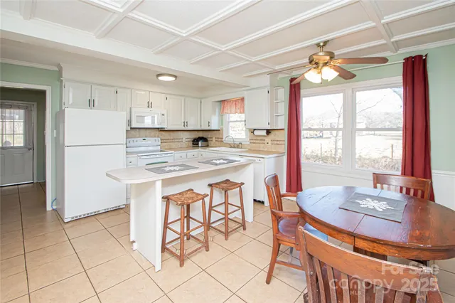 a kitchen with stainless steel appliances granite countertop a stove a refrigerator a sink a dining table and chairs with white cabinets