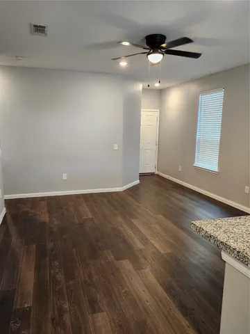 an empty room with wooden floor chandelier fan and windows